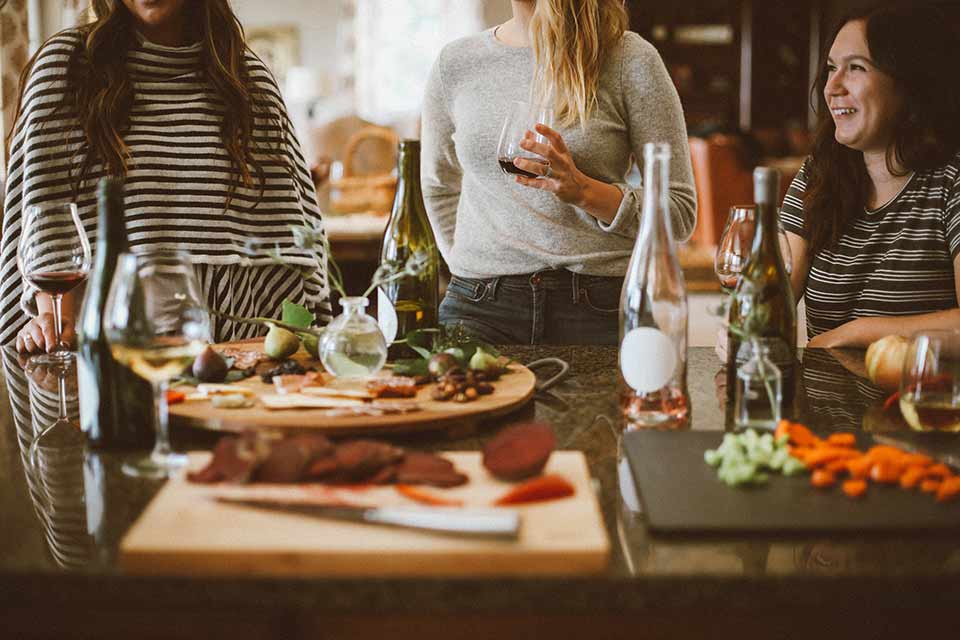 Three women drinking wine while preparing a meal